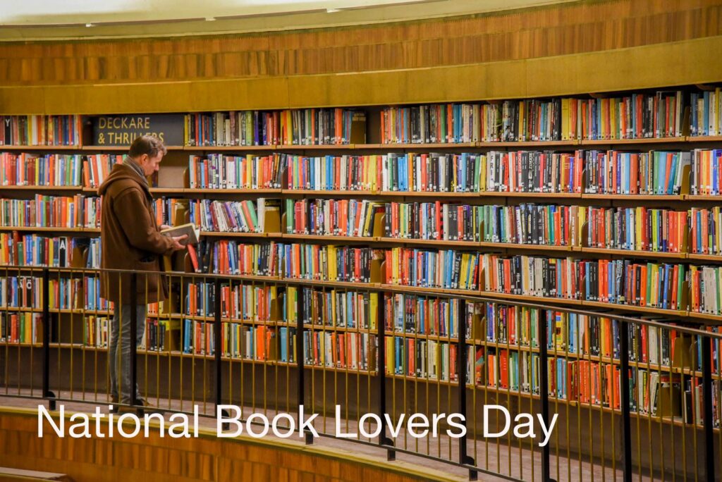 A man stands, paging through a book, in front of 6 rows of upright books. Text: National Book Lovers Day