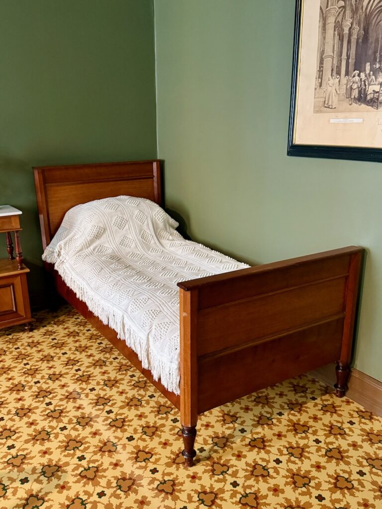 A single bed with wooden frame in the corner of a room with medium green walls.